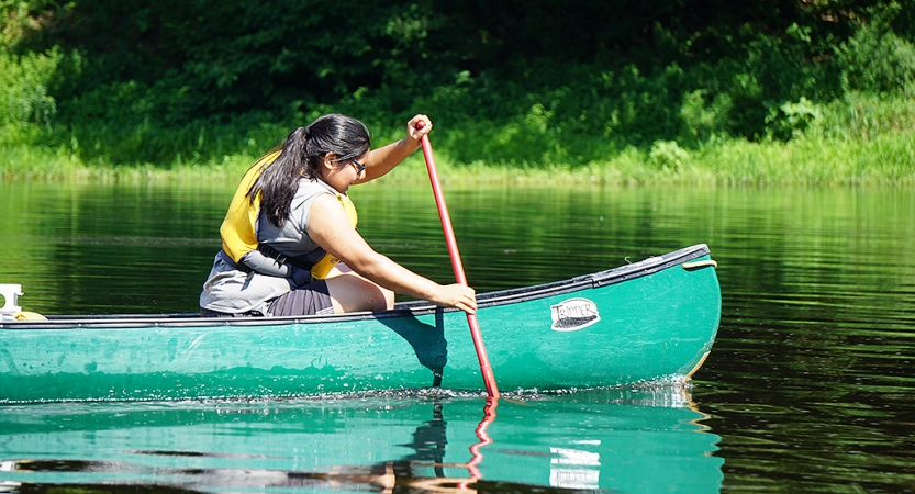 A person wearing a life jacket paddles a canoe